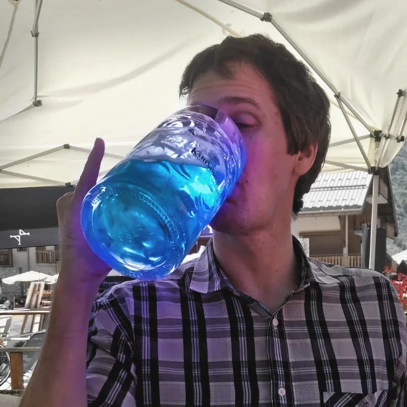 The same man, a mug of electric-blue liquid in hand, index finger raised.